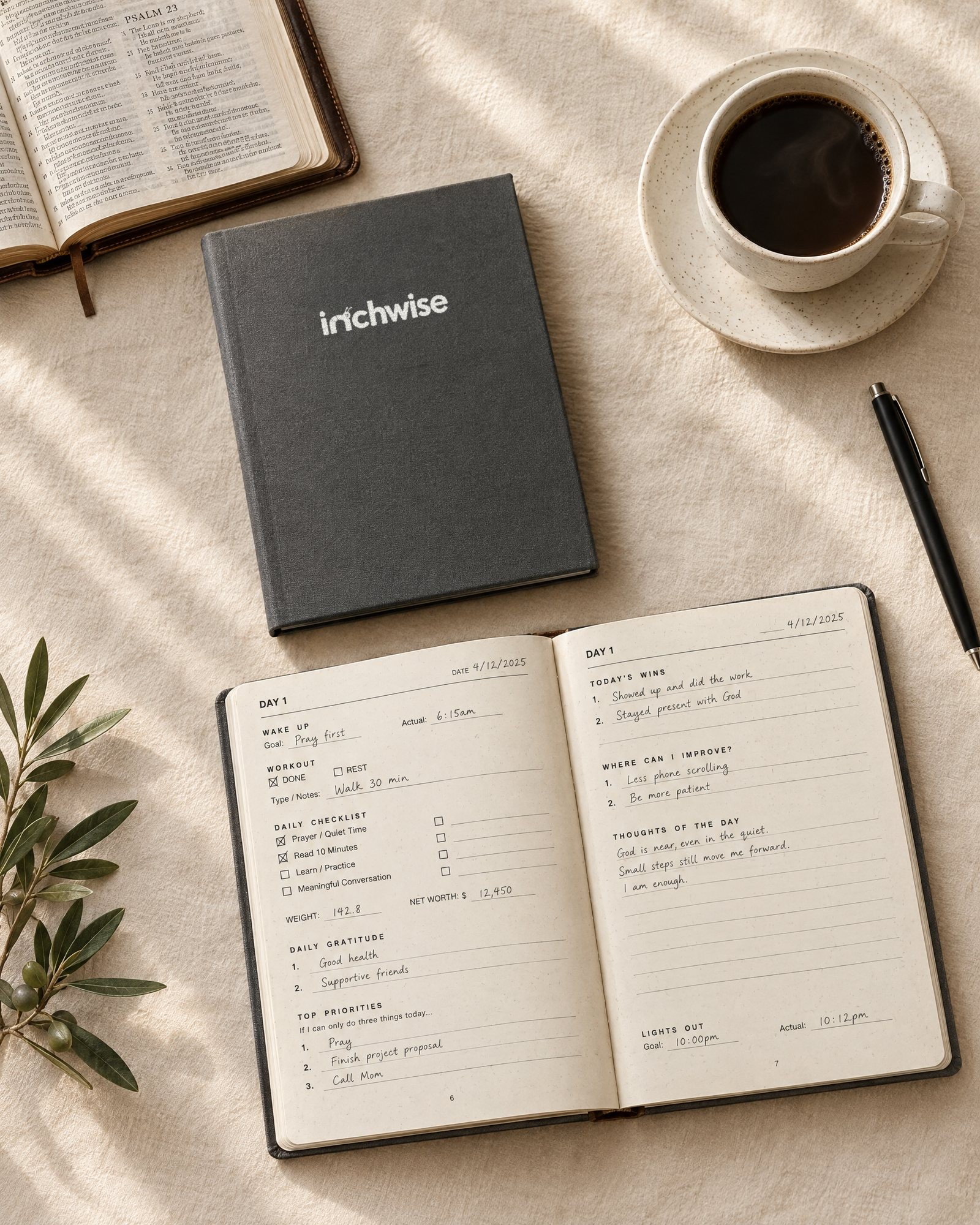 The Inchwise journal closed beside a filled-in open copy, with coffee, a pen, an open Bible and an olive sprig