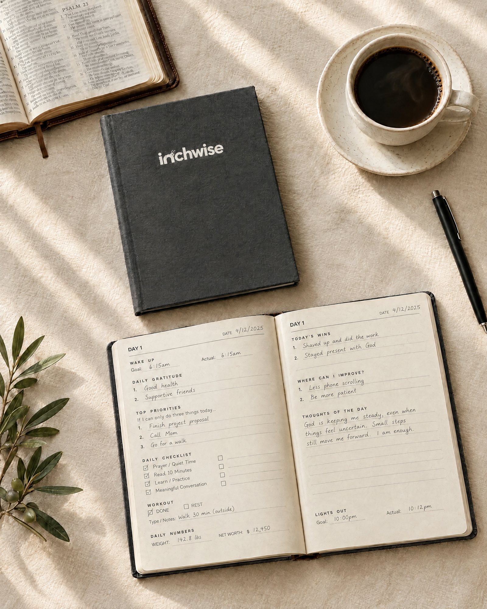 The Inchwise journal closed beside a filled-in open copy, with coffee, a pen, an open Bible and an olive sprig